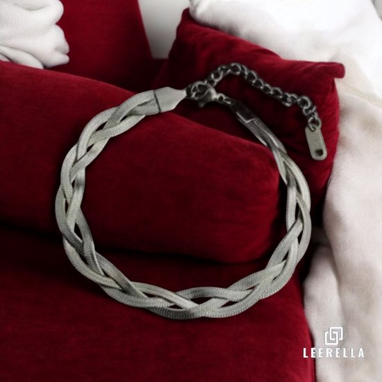 Zilverkleurige, drievoudig gevlochten slangarmband van roestvrij staal, rustend op rode kussens.