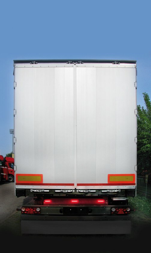 Achterkant van een witte trailer met rode achterlichten en gele reflectoren.