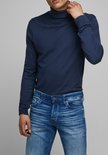 Man met de hand in zijn nek, draagt een strakke donkerblauwe coltrui en een spijkerbroek.