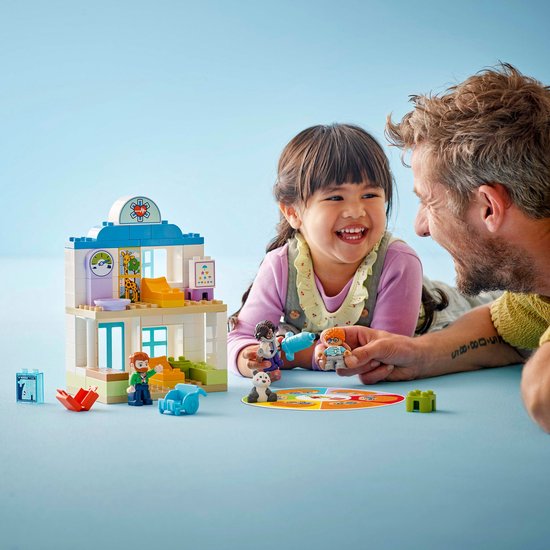 Vader en dochter lachen en spelen met LEGO Duplo dokterscentrum. Op de grond liggen diverse onderdelen.