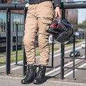 Vrouw op een zebrapad, draagt zandkleurige cargobroek en zwarte laarzen, houdt een helm vast.