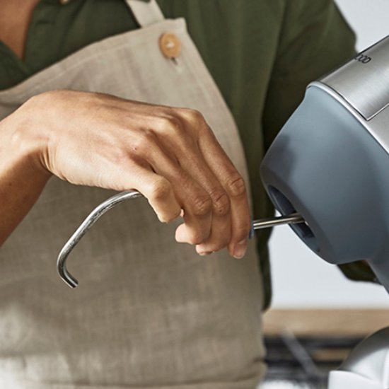 Hand van een vrouw met schort die een deeghaak in een keukenmachine steekt.