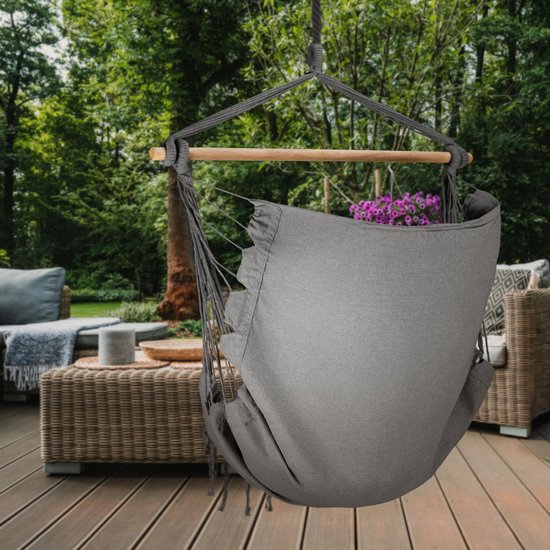 Grijze hangstoel met franjes, op een houten terras.