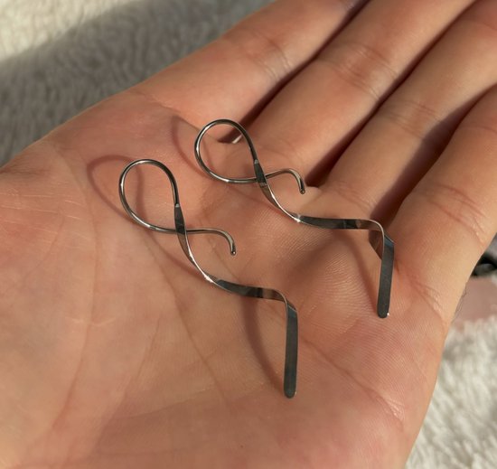 Zilverkleurige spiraal oorbellen in een hand. De oorbellen hebben een gedraaide staafvorm.
