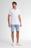 Model draagt witte korte mouw polo shirt met logo op de borst, met lichtblauwe denim short.