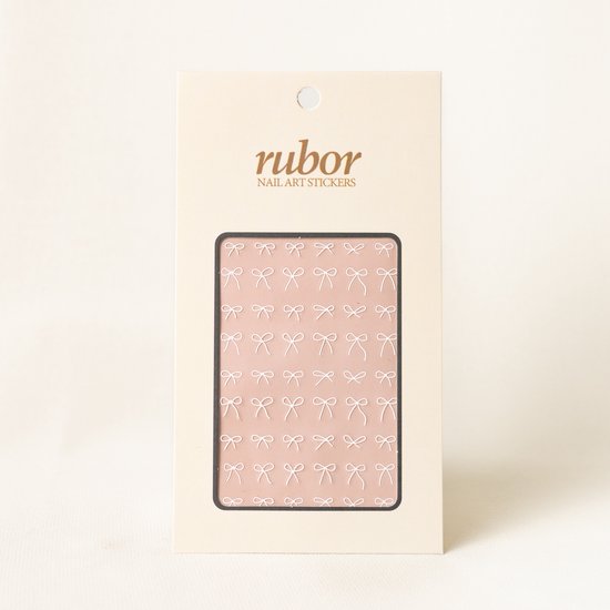 Rubor nail art stickers met witte strikjes op een lichtroze achtergrond.