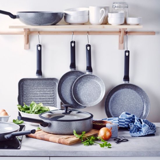 Een keukenopstelling met verschillende BK pannen waaronder een grillpan, koekenpannen en een kookpan, ingrediënten en keukendoeken.