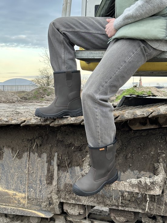 Donkergrijze leren werkschoenen met oranje logo op de zijkant, gedragen met grijze jeans.