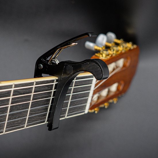 Zwarte gitaarcapo op de hals van een akoestische gitaar, bij de frets.
