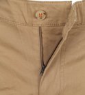 Detail van de sluiting van een lichtbruine chino broek met bruine knoop en rits.
