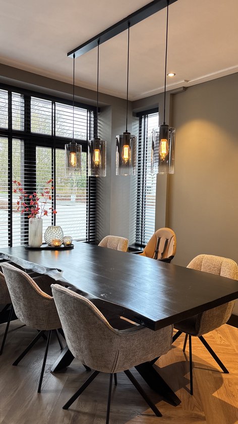 Eettafel in een eetkamer met vijf stoelen en een kinderstoel, met een hanglamp erboven.