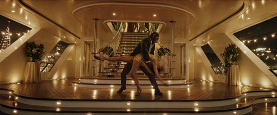 Een aap en een vrouw dansen op een luxe jacht in de nacht, met tafels en een trap op de achtergrond.