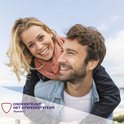 Lachend blond meisje op de rug van een man met baard, tegen een blauwe lucht. Tekst 'ondersteunt het afweersysteem vitamine C'.