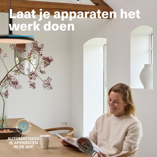 Vrouw leest een tijdschrift aan een houten tafel in een lichte woonkamer. Een vaas met bessen staat op tafel.