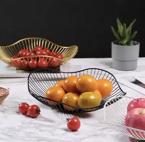 Een gouden fruitschaal gevuld met sinaasappels en een zwarte fruitschaal met tomaten op een marmeren tafel.