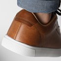 Close-up van de hiel van een bruine leren sneaker van Jack & Jones met witte zool en spijkerbroek.