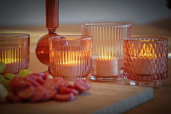 Verschillende glazen windlichten in roze tinten met LED kaarsjes, met fruit op de voorgrond.