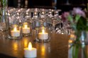 Set van vier LED waxinelichtjes in glazen potjes op een donkere tafel.