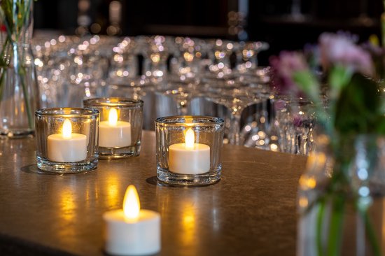 Set van vier LED waxinelichtjes in glazen potjes op een donkere tafel.