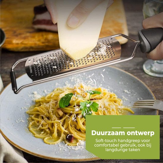 Râpe en acier inoxydable avec manche noir doux au toucher, râpant du fromage sur une assiette de spaghettis, avec citron et herbes.