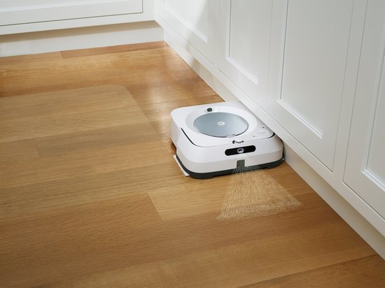 Witte robotdweilrobot reinigt op houten vloer bij witte keukenkastjes.