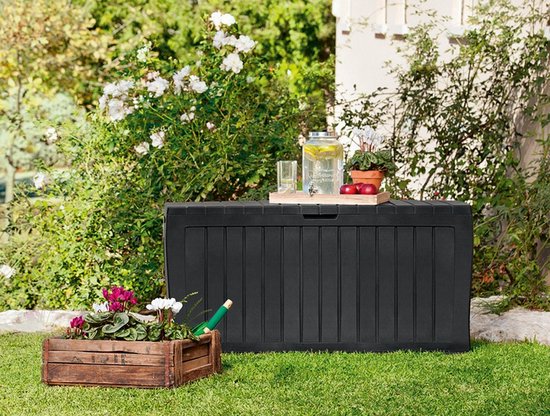 Zwarte opbergbox in een tuin met gras, struiken en een houten plantenbak.