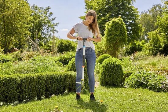 Vrouw met gestreept shirt en jeans onkruid wippend in een tuin met GARDENA onkruidsteker.