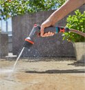 Hand sproeit een tegelvloer met een Gardena spuitpistool.