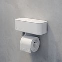 Porte-rouleau toilette blanc Tiger 2-Store avec bac de rangement, monté sur un mur en béton gris.