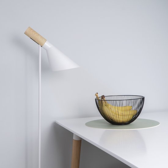 Zwarte metalen fruitschaal met verticale spijlen op een witte tafel naast een witte staande lamp.