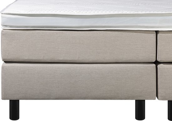 Zijzicht op een beige boxspring met twee lades en zwarte pootjes, met witte matrastop.