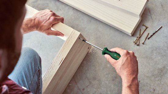 Man met een Bosch schroevendraaier met groen handvat die een schroef in hout draait.