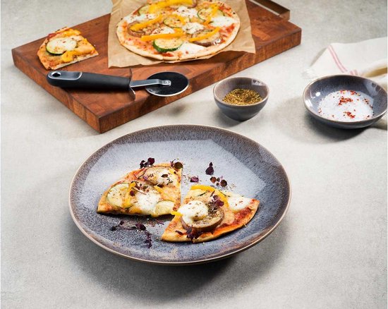 Vegetarische pizza met courgette, aubergine en paprika, gesneden op een bord met een stuk pizza, kruiden en zout.