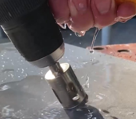 Diamantboormachine die een gat boort in een grijze tegel, met water dat druppelt.