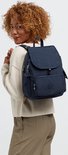 Vrouw met krullend haar draagt een donkerblauwe Kipling rugzak met klep en ritsvak op haar schouder.