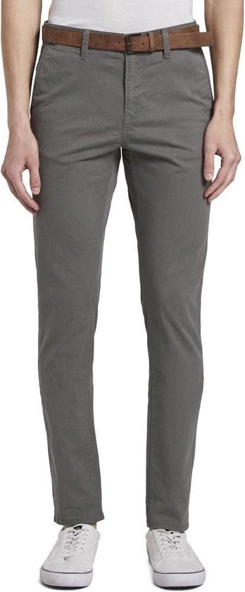 Man in grijze chino met bruine riem en witte sneakers.