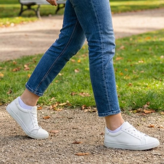 Vrouw met een blauwe jeans en witte sneakers, zomersokken, wandelen in een park.
