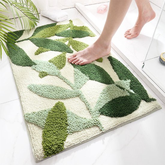 Voet op crèmekleurige badmat met groen bladmotief, antislip, zacht pluche.