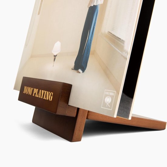 Detail van een vinylhoes op een houten standaard met "NOW PLAYING"-opschrift.