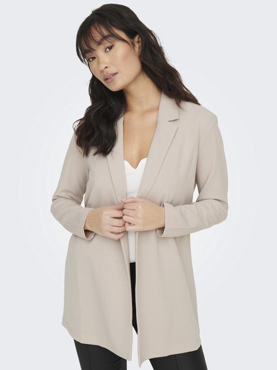 Vrouw met lange, golvende donkere haren in een lange, beige blazer met open voorkant en een witte top.