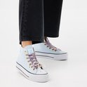 Voeten van vrouw in lichtblauwe hoge sneakers met dikke zolen en panterprint strikken met parels.