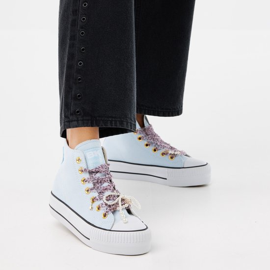 Voeten van vrouw in lichtblauwe hoge sneakers met dikke zolen en panterprint strikken met parels.