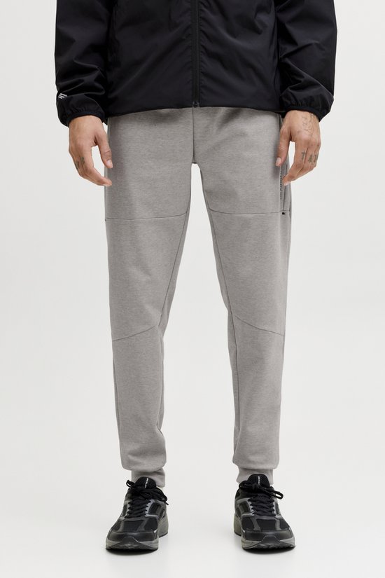 Man draagt een zwarte jas over een grijze joggingbroek met strakke broekspijpen en zwarte sneakers.