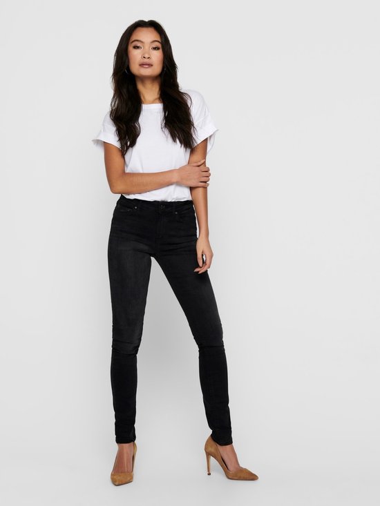 Model met lang, donker haar draagt een strakke zwarte jeans met een witte top.