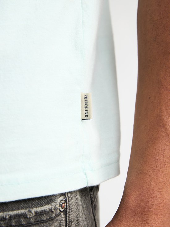 Detail van een lichtgroen T-shirt met een label met 'PETROL IND' erop.