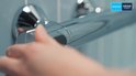 Hand draait aan een thermostaatkraan van een douche, met merklogo's 'QUICKFIX' en 'GROHE'.