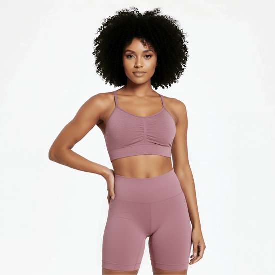 Vrouw met afro haar, van voren gezien, draagt een roze sportbeha met ruching en een roze fietsbroek.