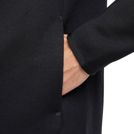 Hand van een man in het vak van een zwarte Nike Tech Fleece hoodie.