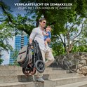 Man draagt een kleine baby op de trap, met de opgevouwen beige Kinderkraft Esme Pro kinderwagen.