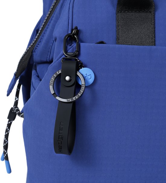 Zwarte sleutelhanger met Hedgren logo aan een blauwe rugzak.